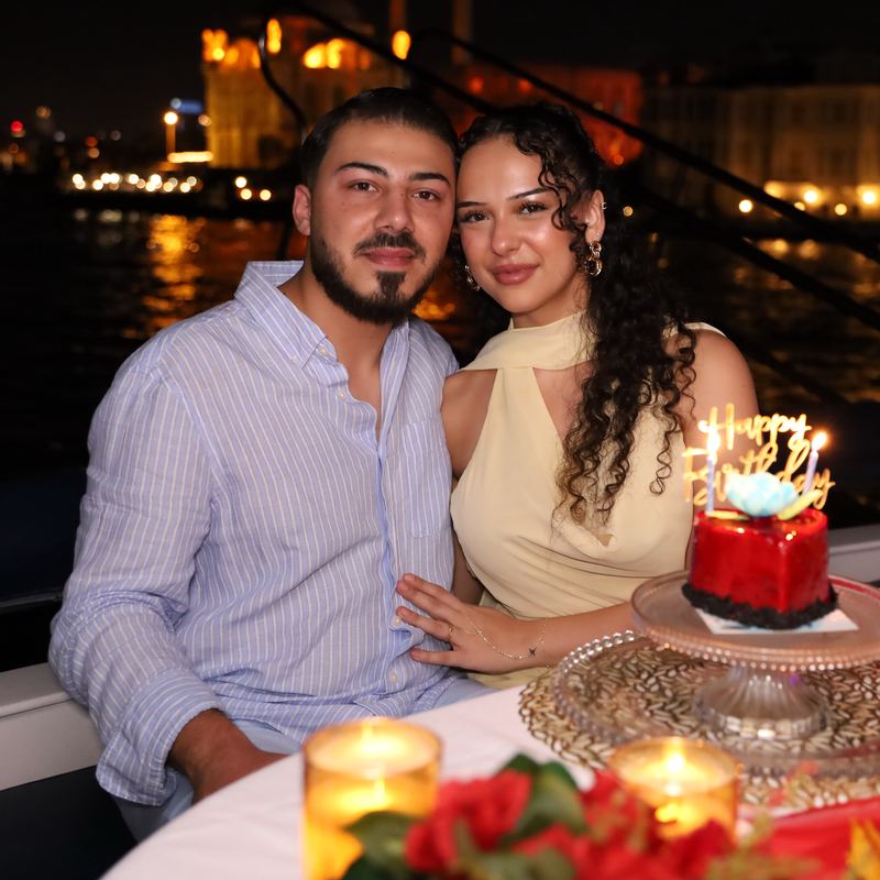 Couple with a birthday cake in front of the lit shoreline