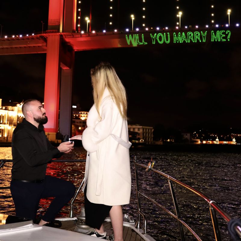 Proposal on one knee on deck, with the laser writing Will you marry me on the Bosphorus Bridge