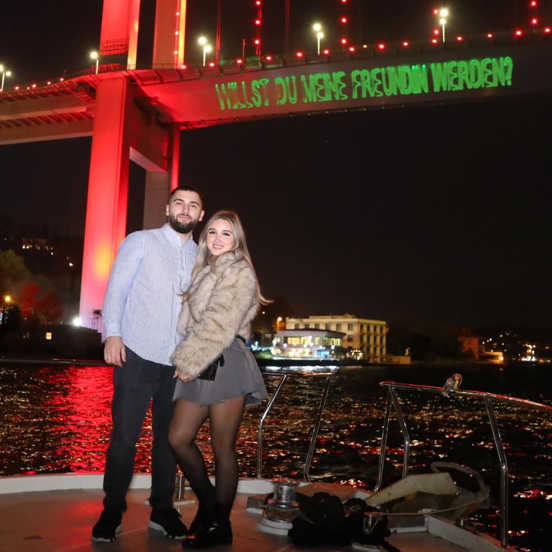 Couple on deck in front of the red-lit bridge with laser writing