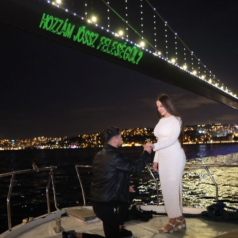 Proposal on the bow of the yacht beneath the green laser writing on the bridge